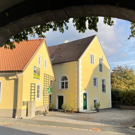 Ein historisches Tor mit Blick auf eine ruhige Straße. Einige farbige Häuser und viel Grün umgeben den Eingang. | © Ferienwohnungen Reiböck