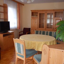 Ein gemütliches Wohnzimmer mit einem runden Tisch und einem Fernseher. Die Möbel sind aus Holz und es gibt eine große Pflanze auf dem Tisch.