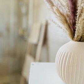 Eine stilvolle Vase mit Trockenblumen steht auf einem Tisch. Im Hintergrund ist eine Dusche und ein Holzstuhl zu sehen. | © Ferienwohnung Vinestia