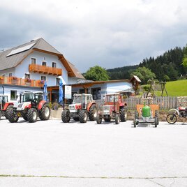 Ein Bauernhof mit mehreren Traktoren vor einem großen Gebäude. Im Hintergrund sind grüne Wiesen und Bäume sichtbar. | © Gasthaus Sallegger-Falkenbauer