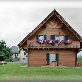 Ein charmantes Holzhaus mit einem Balkon voller bunter Blumen. Umgeben von einer grünen Wiese und Bäumen bietet es eine gemütliche Atmosphäre. | © Frühstückspension Liebmann