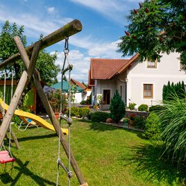 Ein schöner Garten mit einer Schaukel und einer Rutsche. Im Hintergrund steht ein helles Haus mit grünen Pflanzen. | © Oliver Meyer
