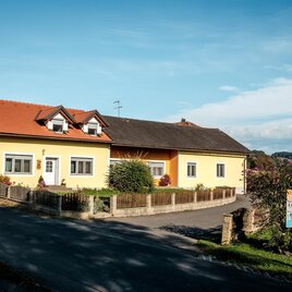Ein gelbes Haus mit rotem Dach befindet sich an einer ruhigen Straße. Es hat einen gepflegten Garten und eine schöne Aussicht auf die Umgebung. | © M Effekt