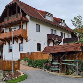 Ein charmantes Haus mit Balkon und einem gepflegten Garten. Der Weg führt vorbei an einer harmonischen Landschaft mit einem Holzsteg. | © Papst Rene
