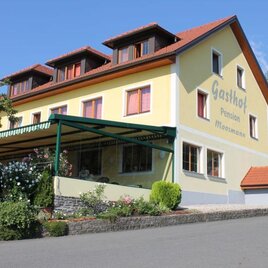 Ein gemütlicher Gasthof mit gelber Fassade und mehreren Fenstern. Umgeben von grünen Pflanzen bietet er eine einladende Atmosphäre. | © Hotel-Pension Moosmann | Fam. Moosmann