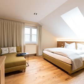 Ein modernes Hotelzimmer im Genussgut Krispel mit einem Doppelbett und einem gemütlichen Sessel. Große Fenster und helles Holz sorgen für eine freundliche Atmosphäre. | © Genussgut Krispel