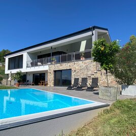 Ein modernes Haus mit einer Terrasse und einem Pool. Die Umgebung ist grün und einladend.