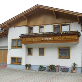 A traditional, well-designed house with a large wooden balcony. Flowers adorn the entrance area and the windows.