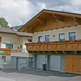 Ein charmantes Haus mit Holzverzierungen und Balkonen, umgeben von einer ruhigen Umgebung. Der Himmel ist teils bewölkt, was der Atmosphäre eine entspannte Stimmung verleiht.