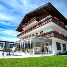 Ein modernes Gebäude im alpinen Stil mit Balkonen, die mit Blumen geschmückt sind. Der Gartenbereich bietet Terrasse und Sitzgelegenheiten im Freien.