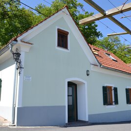 Ein charmantes, hellgrünes Haus mit einem roten Ziegeldach und weißen Fenstern. Umgeben von Bäumen und einer klaren blauen Himmel. | © Albert Gutmann