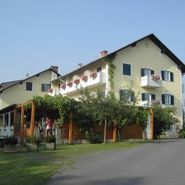 Ein zweigeschossiges Gebäude mit Balkonen und Blumenkästen. Umgeben von grünen Pflanzen und einem Weg, der zu dem Gebäude führt. | © Gasthof Pension Kulmberghof