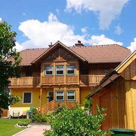 A beautiful, traditional house with wooden cladding and several windows. The sky is clear and there are green plants around the building.