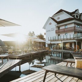 Ein stilvolles Hotel mit einem Poolbereich und Sonnenschirmen. Die Sonne scheint auf die Holzterrassen und schafft eine entspannte Atmosphäre. | © Karl Schrotter und cmvisuals
