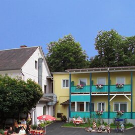 Ein charmantes Gästehaus mit bunten Fassaden und einem einladenden Innenhof. Die Umgebung ist grün und freundlich, ideal für einen erholsamen Aufenthalt. | © Grünbichler