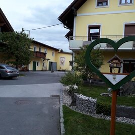 A cozy courtyard with yellow buildings and lots of green plant growth. In the foreground is a heart-shaped sign. | © Obsthof Glück