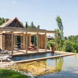 Ein modernes Haus aus Stein mit Holzveranda und Pool. Es liegt in einer grünen Umgebung mit Blick auf die Natur. | © PURESleben Ferienhäuser l Dietmar Silly