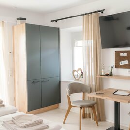 A modern room with two beds, a table, and a television. The windows are fitted with curtains, and the room feels friendly and inviting. | © youvia.creations