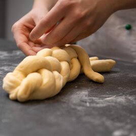 Eine Person formt einen geflochtenen Teig auf einer Arbeitsfläche. Der Teig ist hell und weich, bereit zum Backen. | © Pension Cäcilia