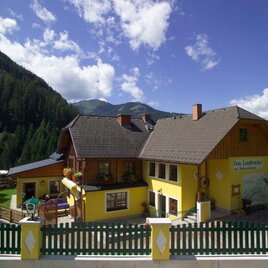 Ein charmantes gelbes Haus inmitten einer malerischen Berglandschaft. Der Himmel ist klar und die Natur umgibt das Gebäude.