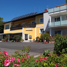 Ein hübsches Gebäude mit gelber Fassade und Balkonen. Der Garten ist mit bunten Blumen und grünen Pflanzen gestaltet. | © Pension Raabtal