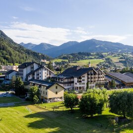 A picturesque mountain landscape with green meadows and modern chalets. In the background, majestic mountains and a clear sky can be seen. | © Harald Steiner
