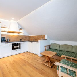Eine moderne Küche mit Holzfußboden und einem gemütlichen Aufenthaltsbereich. Die Einrichtung ist hell und einladend. | © www.mynests.at