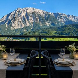 <p>Ein eleganter Essbereich auf dem Balkon mit Blick auf den majestätischen Grimming. Der Tisch ist schön gedeckt und die Umgebung ist grün und malerisch.</p> | © Urlaub in Tauplitz - Design Apartment Grimmingblick, www.urlaubintauplitz.com