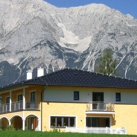 A stylish yellow house with a black roof is set against an impressive mountain landscape. The majestic mountains create a stunning backdrop.