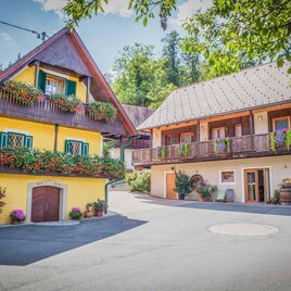 Zwei charmante Häuser in einer malerischen Straße. Das gelbe Haus hat bunte Blumenfenster, während das andere einen gemütlichen Balkon hat. | © Weingut Albrecher vlg. Sraka | Fam. Albrecher