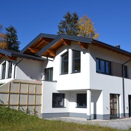 A modern house with large windows in a rural setting. The façade is bright and the architecture is contemporary.