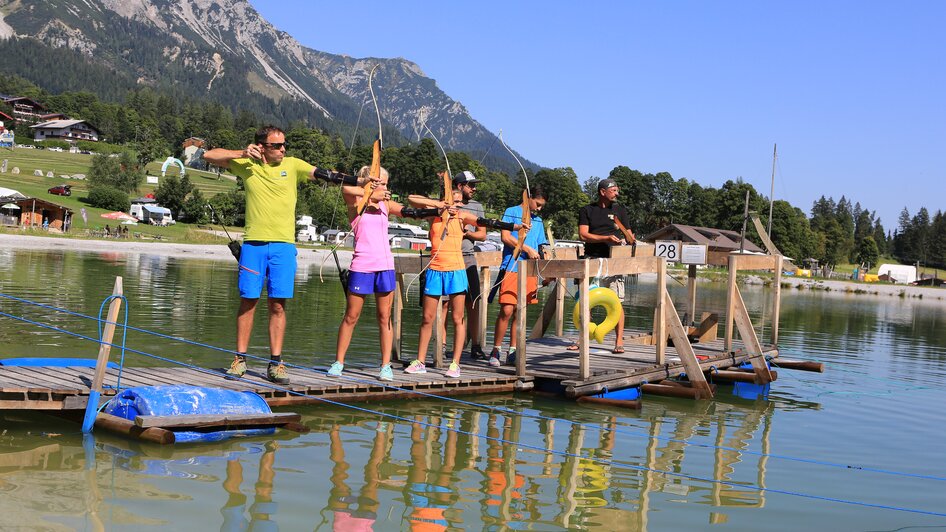 Gruppe am Bogenschießen steht auf einem Steg im Wasser.  | © Erlebnis Rittisberg