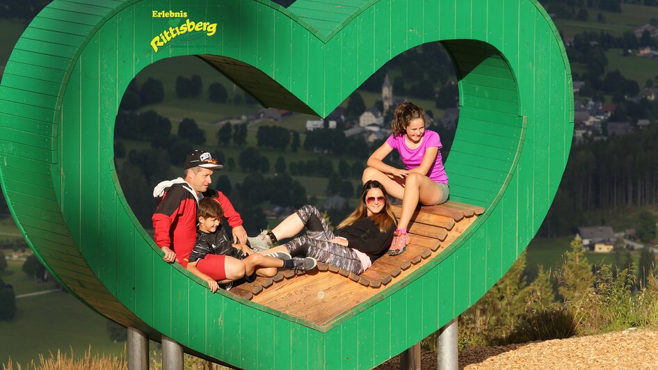 Familie sitzt in der Mitte des grünen Herzens.  | © Erlebnis Rittisberg